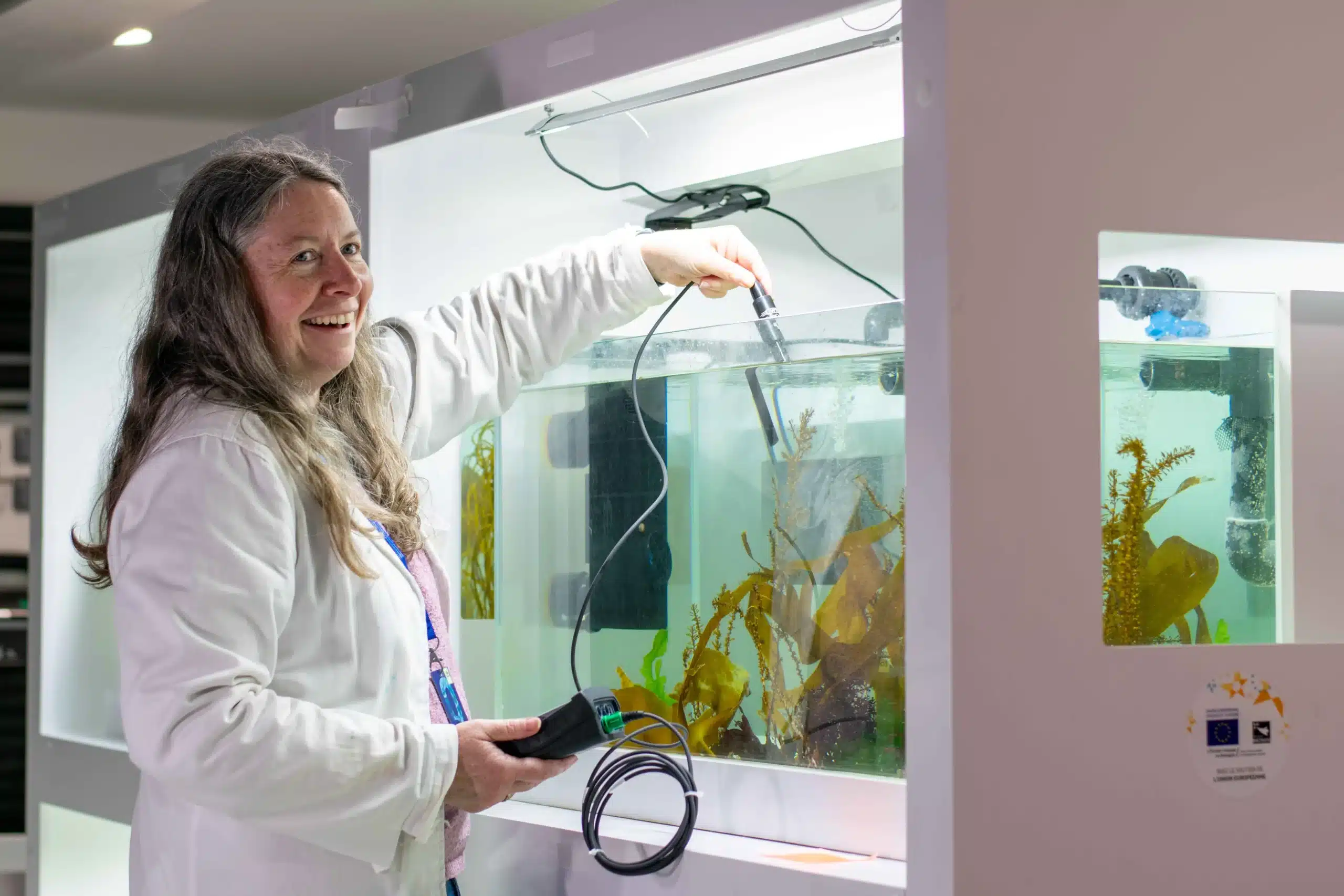Solène Connan, enseignante chercheur du projet ALCID, se tenant en blouse au dessus d'un bassin avec une sonde permettant de mesurer la température.